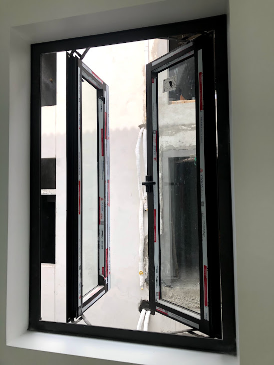 Cửa sổ nhôm kính màu đen mở quay hai cánh nhìn ra giếng trời trong nhà đang xây dựng